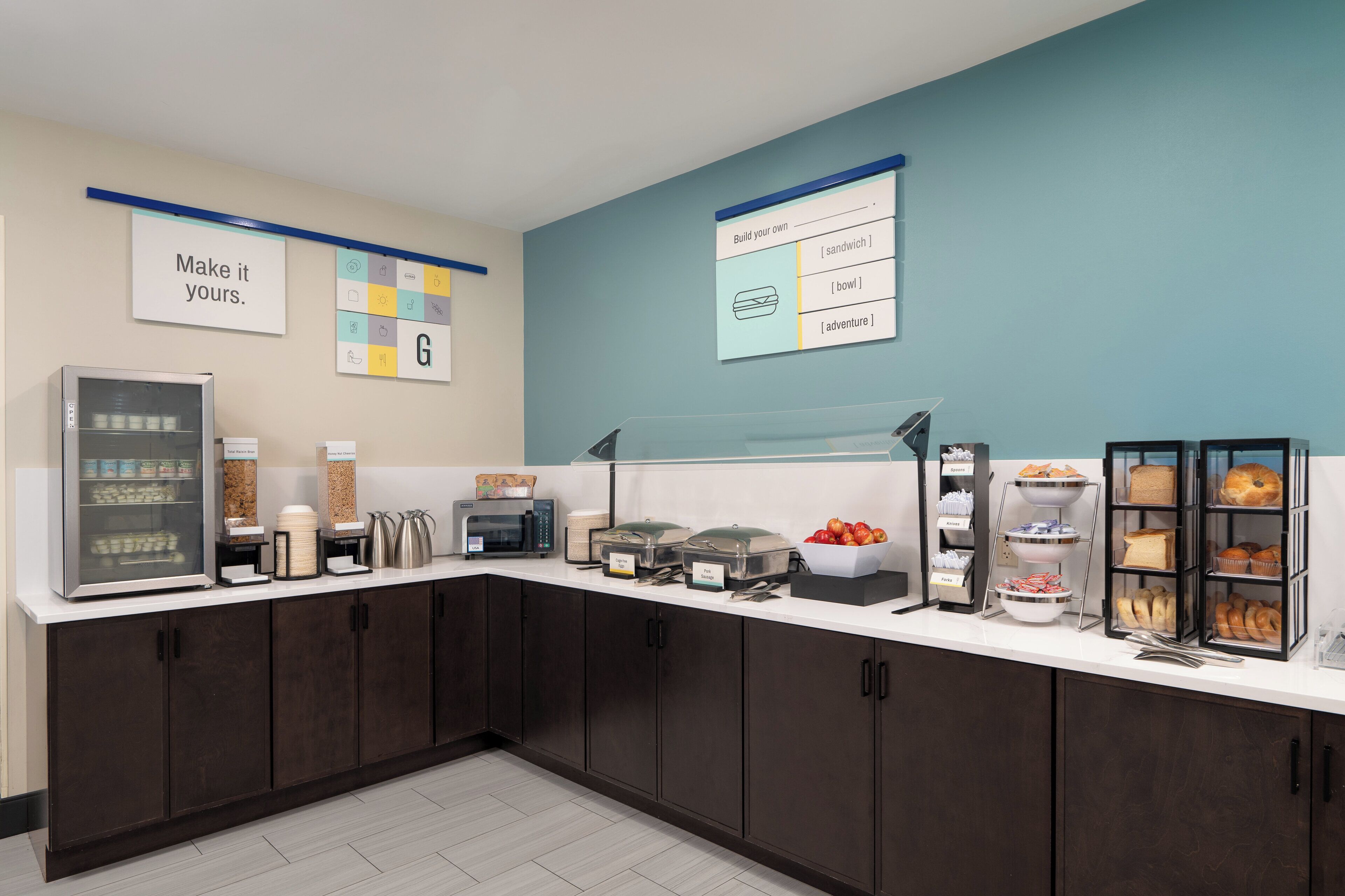 A self-service breakfast area with a refrigerator, coffee maker, and various food containers.