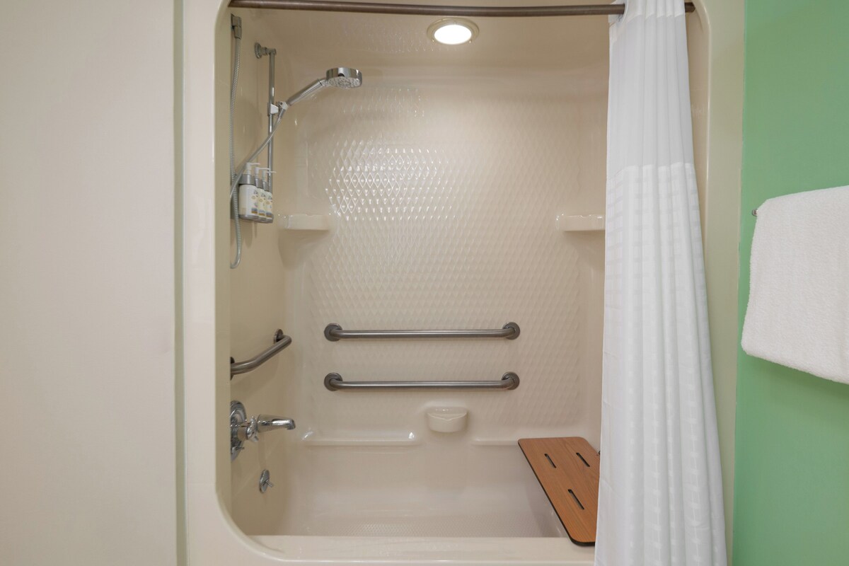 Une salle de bain équipée d’une baignoire, de barres d’appui, d’un pommeau de douche et d’un porte-serviettes.