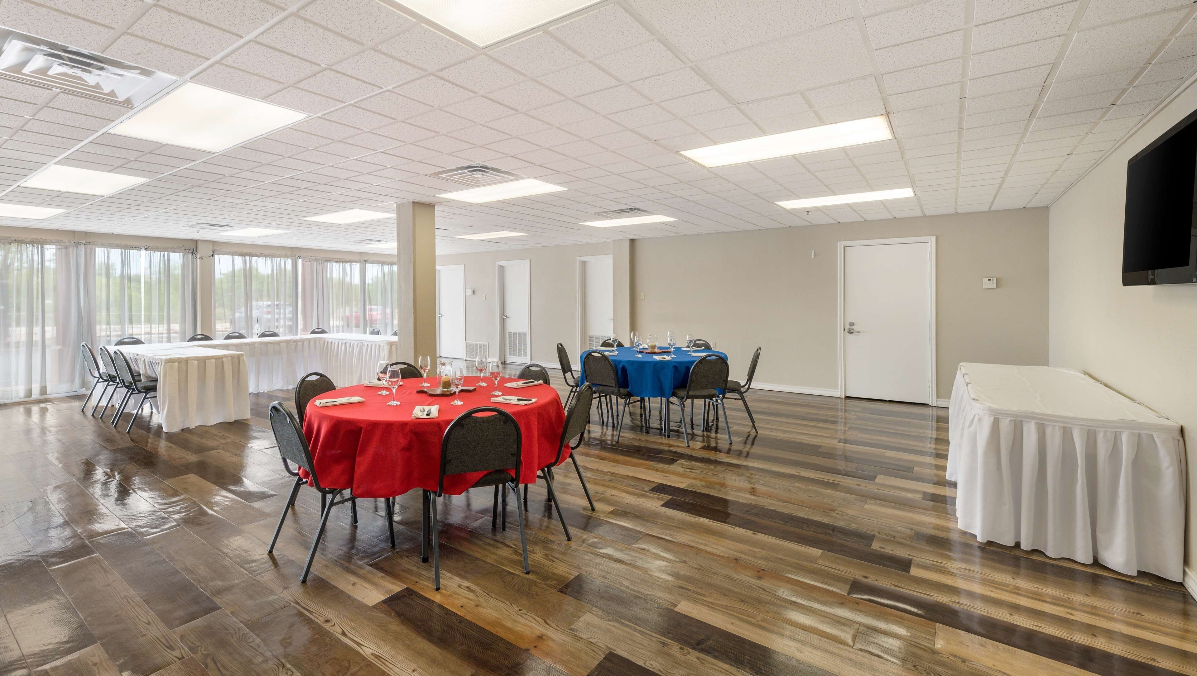 A spacious room with two round tables, one covered with a red tablecloth and the other with a blue tablecloth, both set with chairs and glassware.