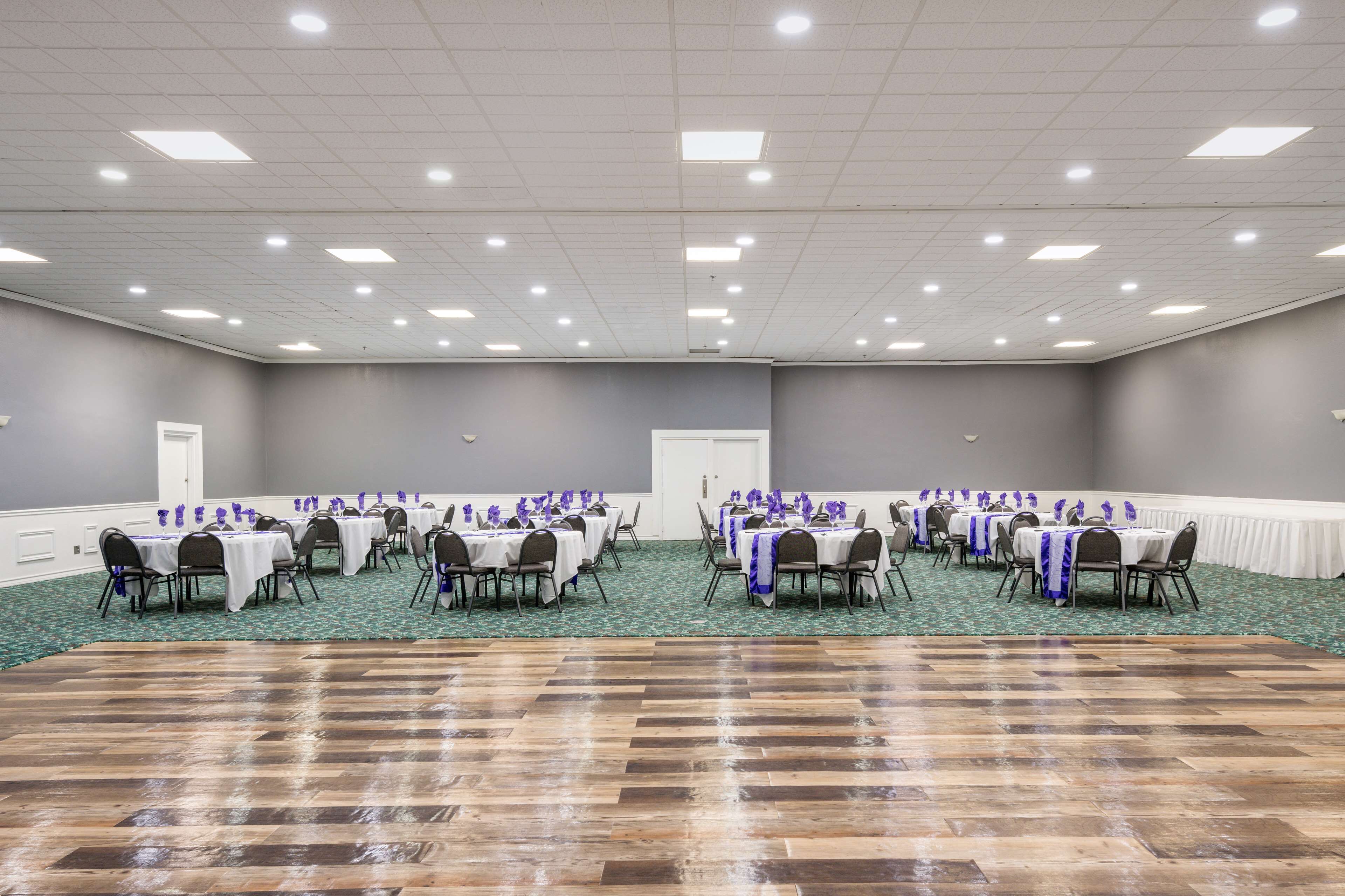 A large conference room with multiple tables and chairs, carpeted floor, and ceiling lights.