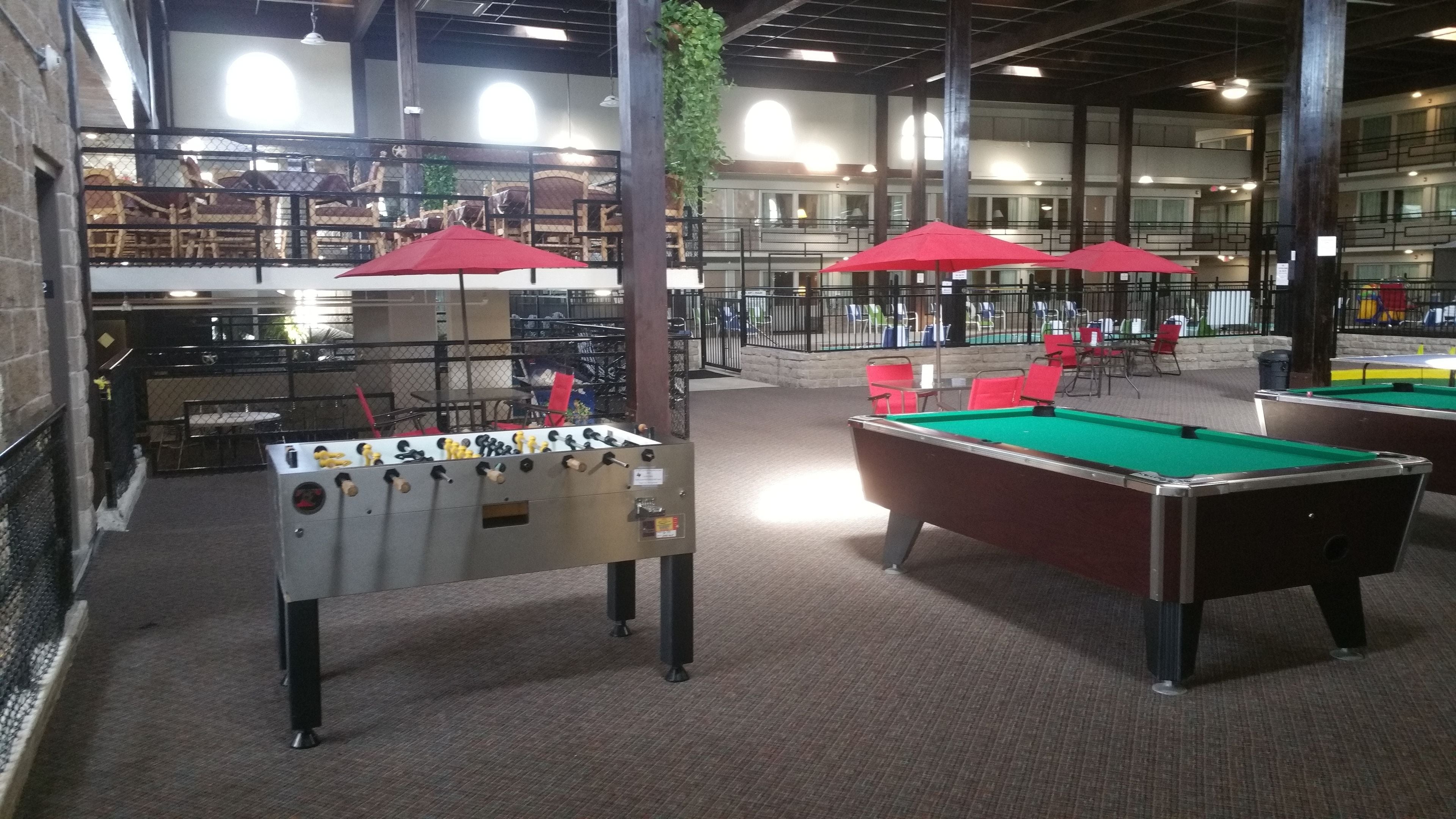 A recreational area with foosball tables and pool tables, surrounded by red umbrellas and seating.