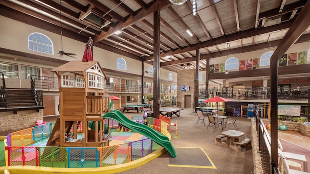 Zona de juegos interior con tobogán, casita y mesas para comer.