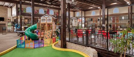 A children's play area with a slide, play structures, and a green turf surface.