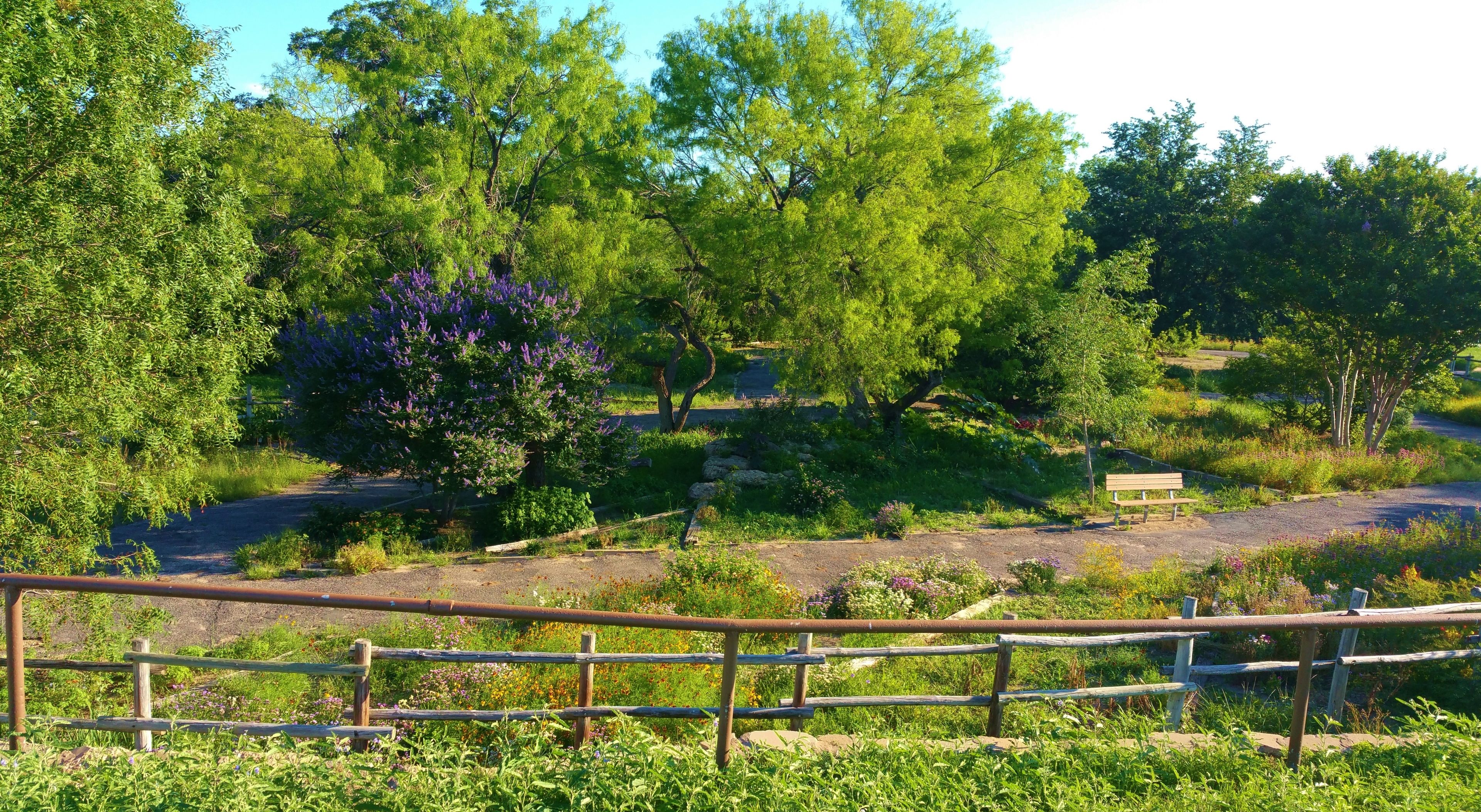 Paisaje natural con un sendero de grava, valla de madera y un banco.