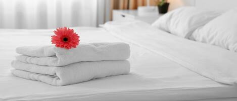 Un lit bien fait, avec des serviettes blanches pliées et une fleur rouge posée sur le dessus.