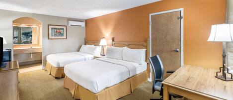 A hotel room with two beds, a desk, a chair, a TV, and a bathroom visible through an arched doorway.