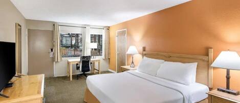 A hotel room with a large bed, two bedside tables with lamps, a desk with a chair, a TV, and a window with curtains.