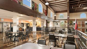 A spacious indoor dining area with high ceilings and large windows, featuring multiple dining tables and chairs.