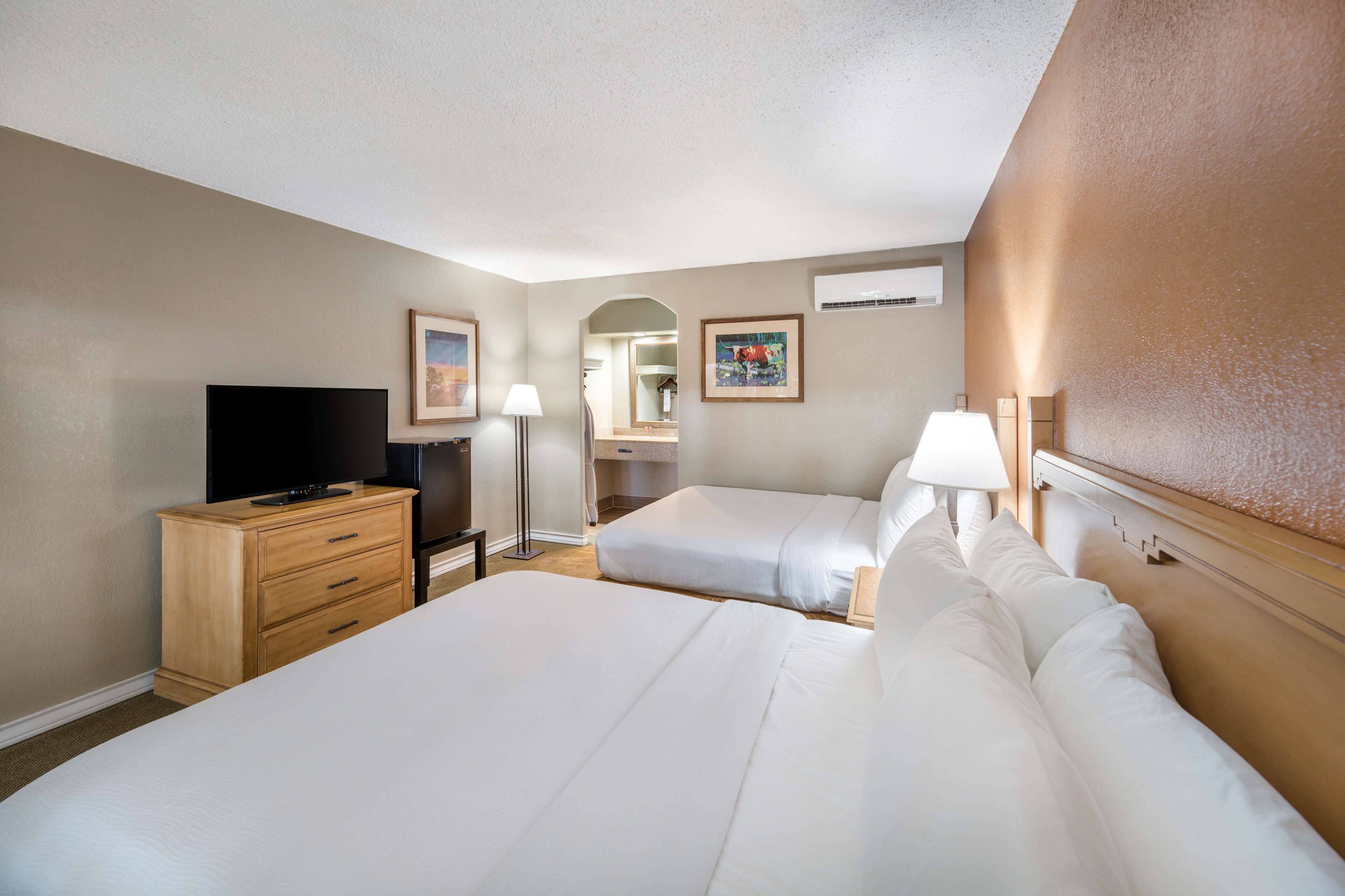 A hotel room with two beds, a TV, a dresser, and a lamp.