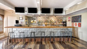 Una zona de bar con mostrador de madera, taburetes de metal y una variedad de botellas.