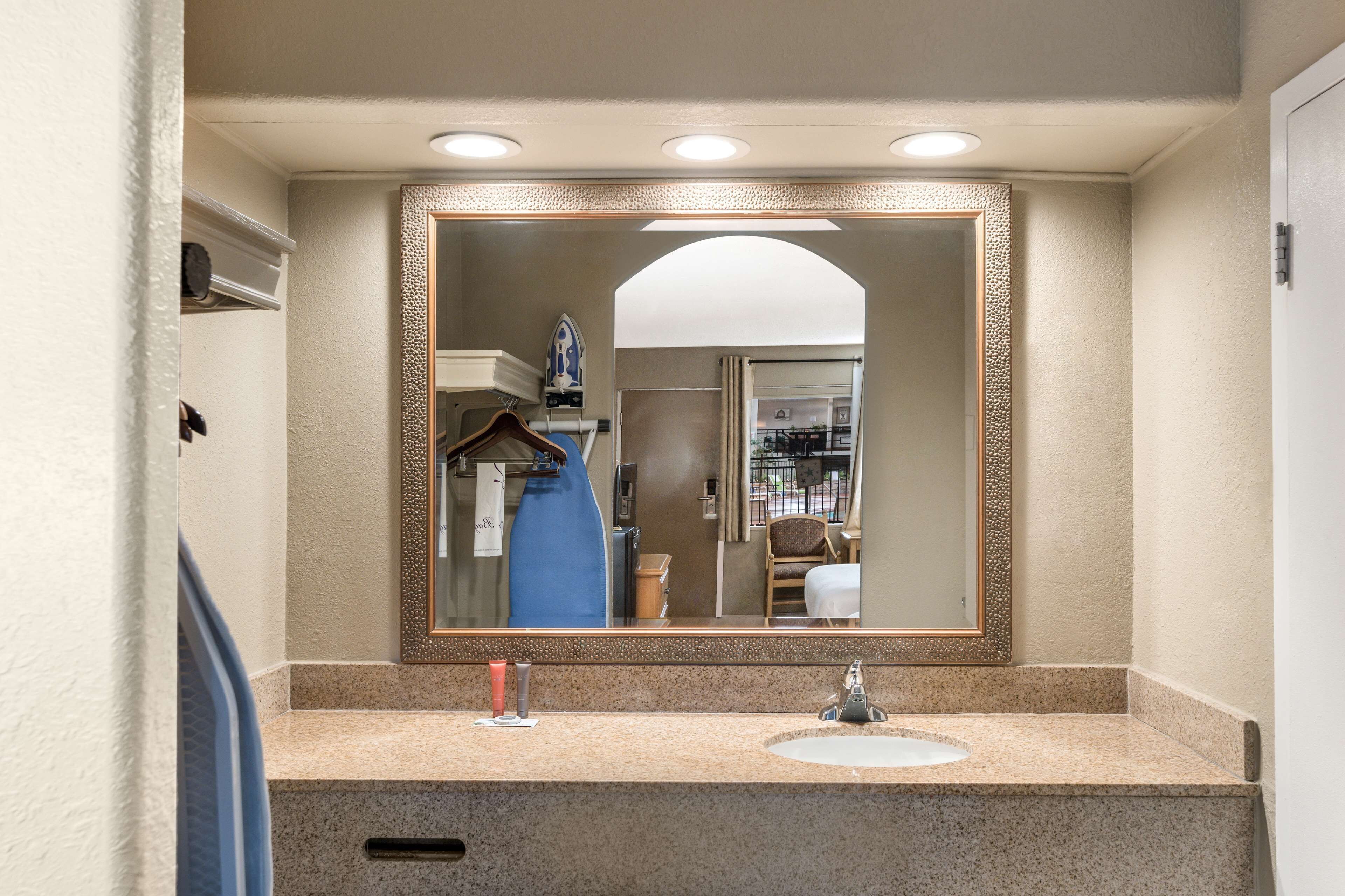 A bathroom with a granite countertop, a sink, and a large mirror with a decorative frame.