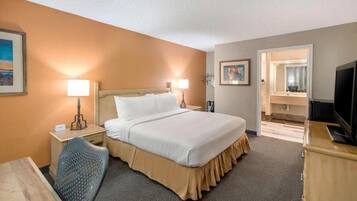 A hotel room with a large bed, two bedside lamps, a desk with a chair, a television, and a bathroom visible through an open door.