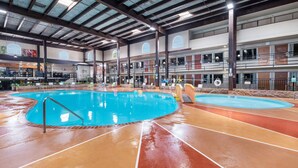 Una piscina interior con varias pistas de natación, una terraza con sol y un edificio de varios niveles con balcones.