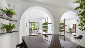 A piano in a spacious room with white walls, arched doorways, and shelves with potted plants. - Hotel Villa Durrueli Resort & Spa (Ischia)