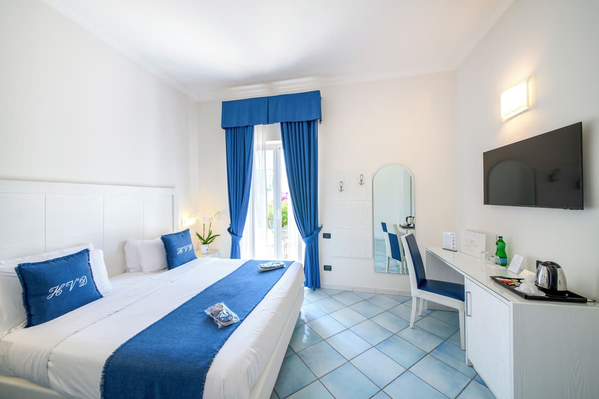 A hotel room with a bed, a desk, a chair, a mirror, and a window with curtains.