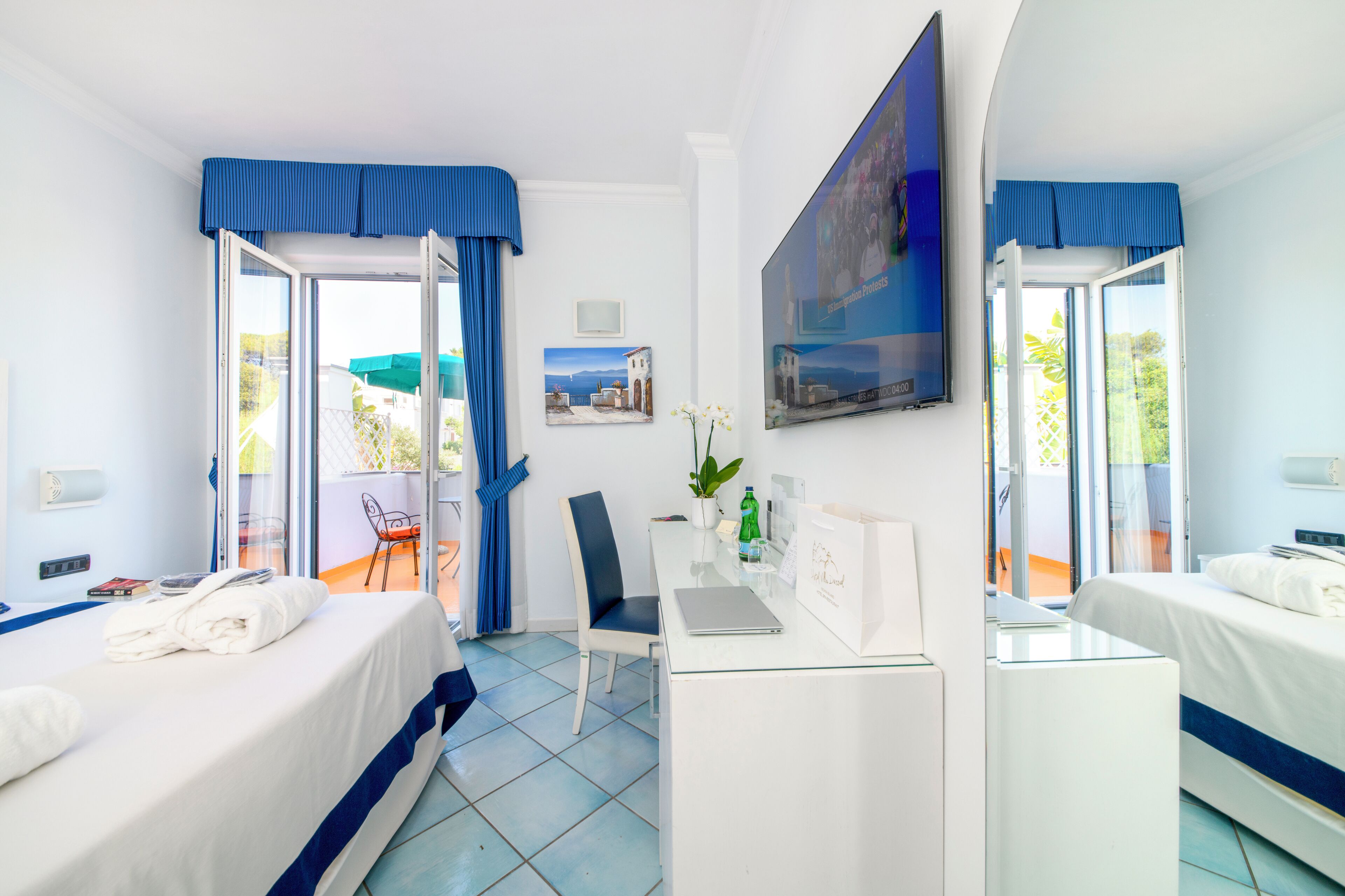 A hotel room with two beds, a desk, a chair, a laptop, and a window with curtains.