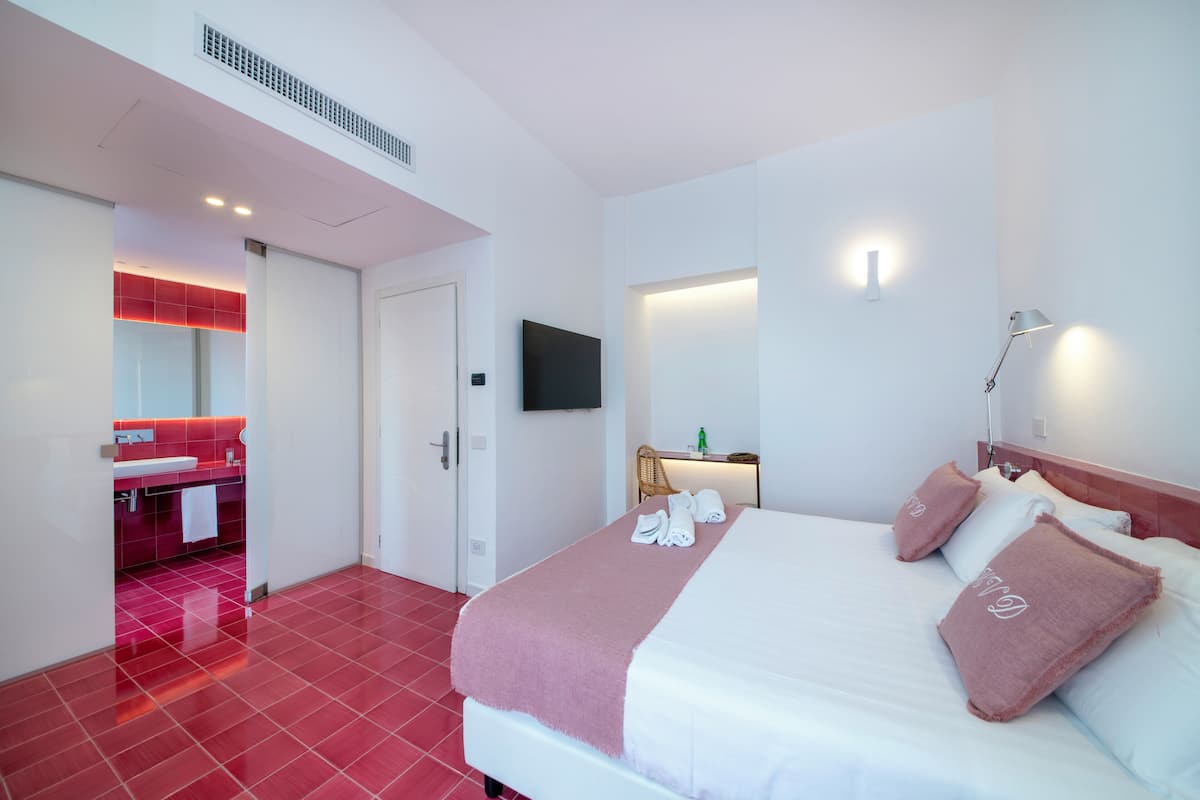 A hotel room with a bed, a TV, a bathroom with a red-tiled floor, and a white door.