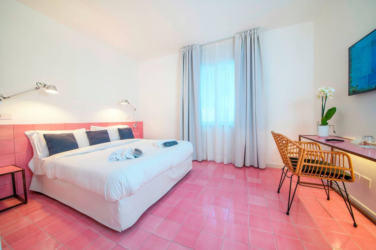 A hotel room with a bed, a desk with a chair, a lamp, and a window with curtains.