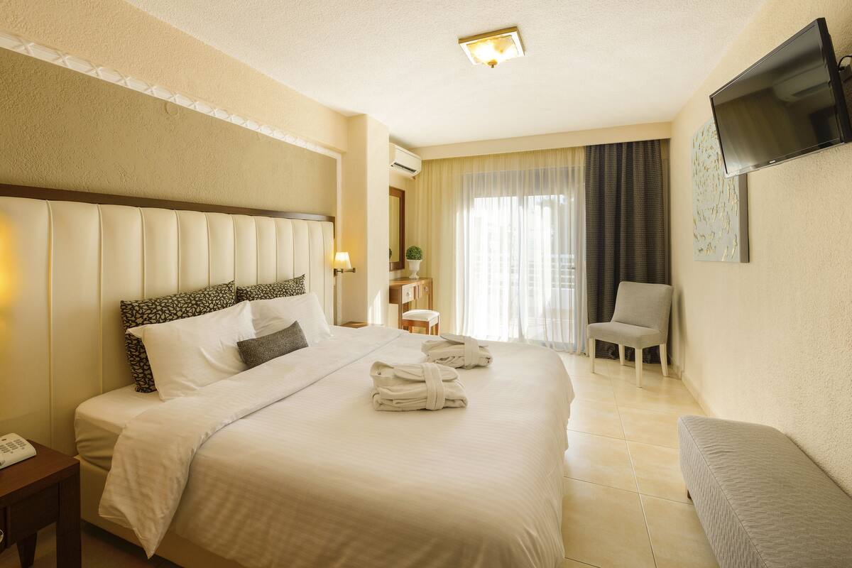 Hotellihuone, jossa on suuri sänky, yöpöydällä lamput, kirjoituspöytä puhelimineen, tuoli ja seinälle asennettu litteänäyttöinen televisio.