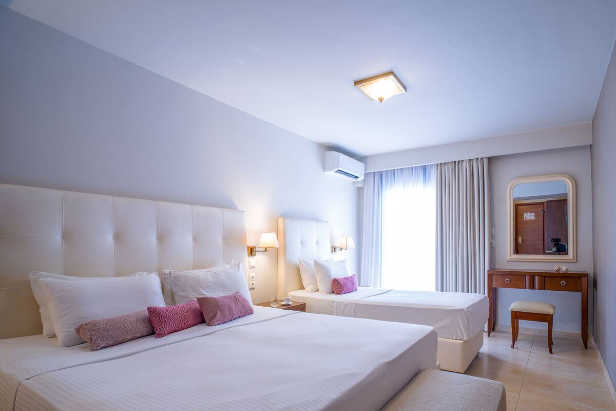 Hotellihuone, jossa on kaksi sänkyä, peilillä varustettu meikkipöytä ja kattovalaisin.