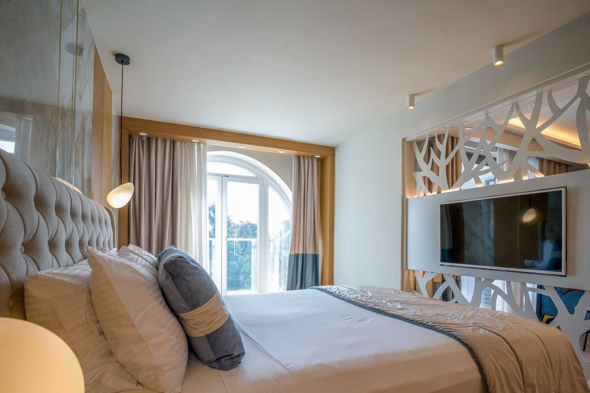 Moderni hotellihuone, jossa on suuri sänky, seinälle asennettu televisio ja ikkuna, jossa on verhot.