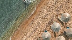 An aerial view of a beach with clear water, a sandy shore, and several beach umbrellas. - Secret Paradise Hotel & Spa (Nea Propontida)