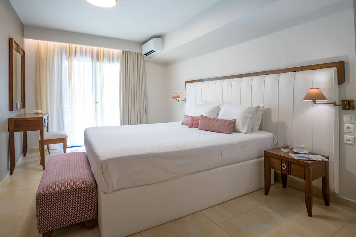 Hotellihuone, jossa on suuri sänky, yöpöydät, työpöytä ja ikkuna, jossa on verhot.