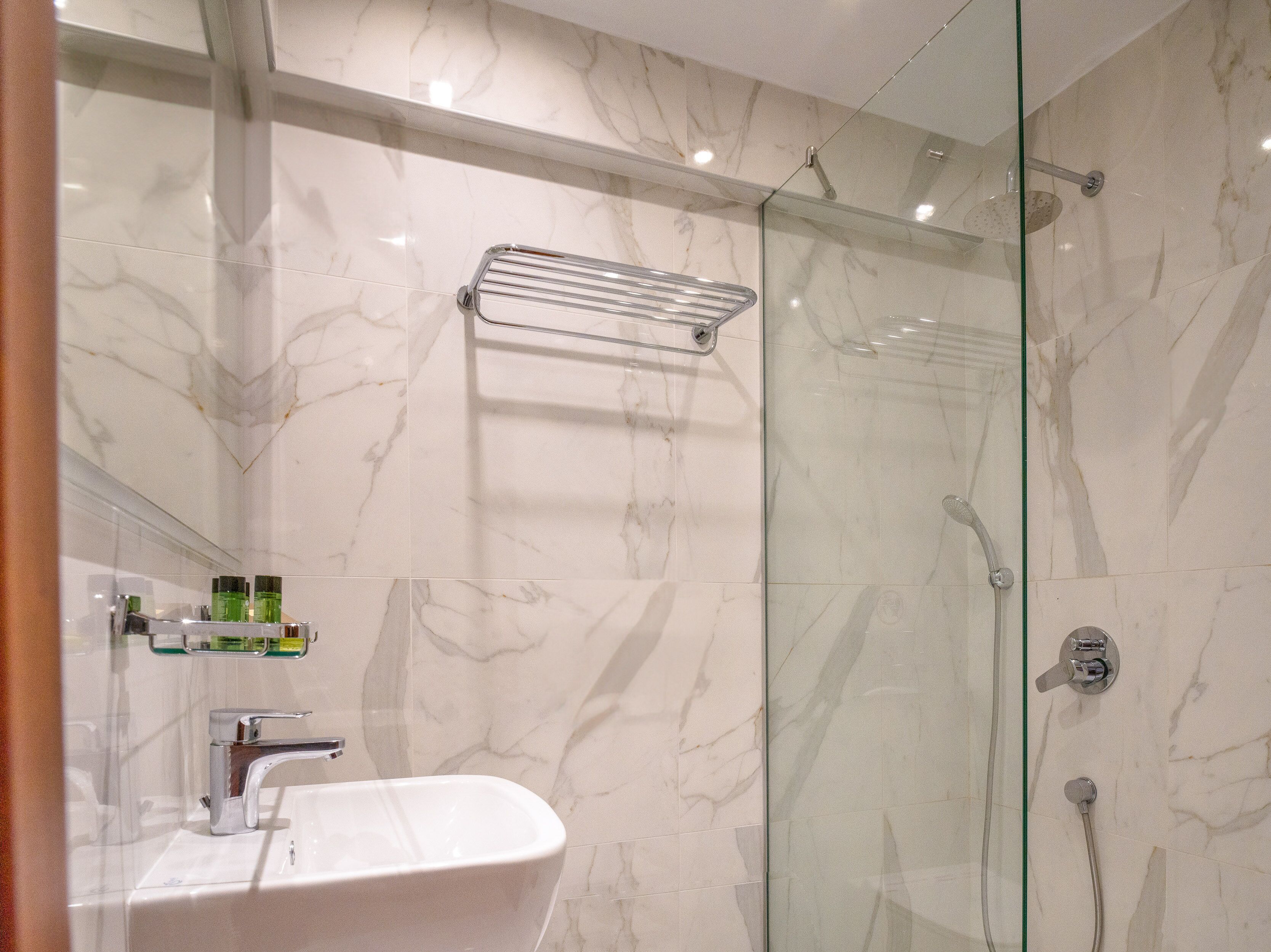 A modern bathroom with a glass-enclosed shower, a white sink, and a marble-tiled wall.