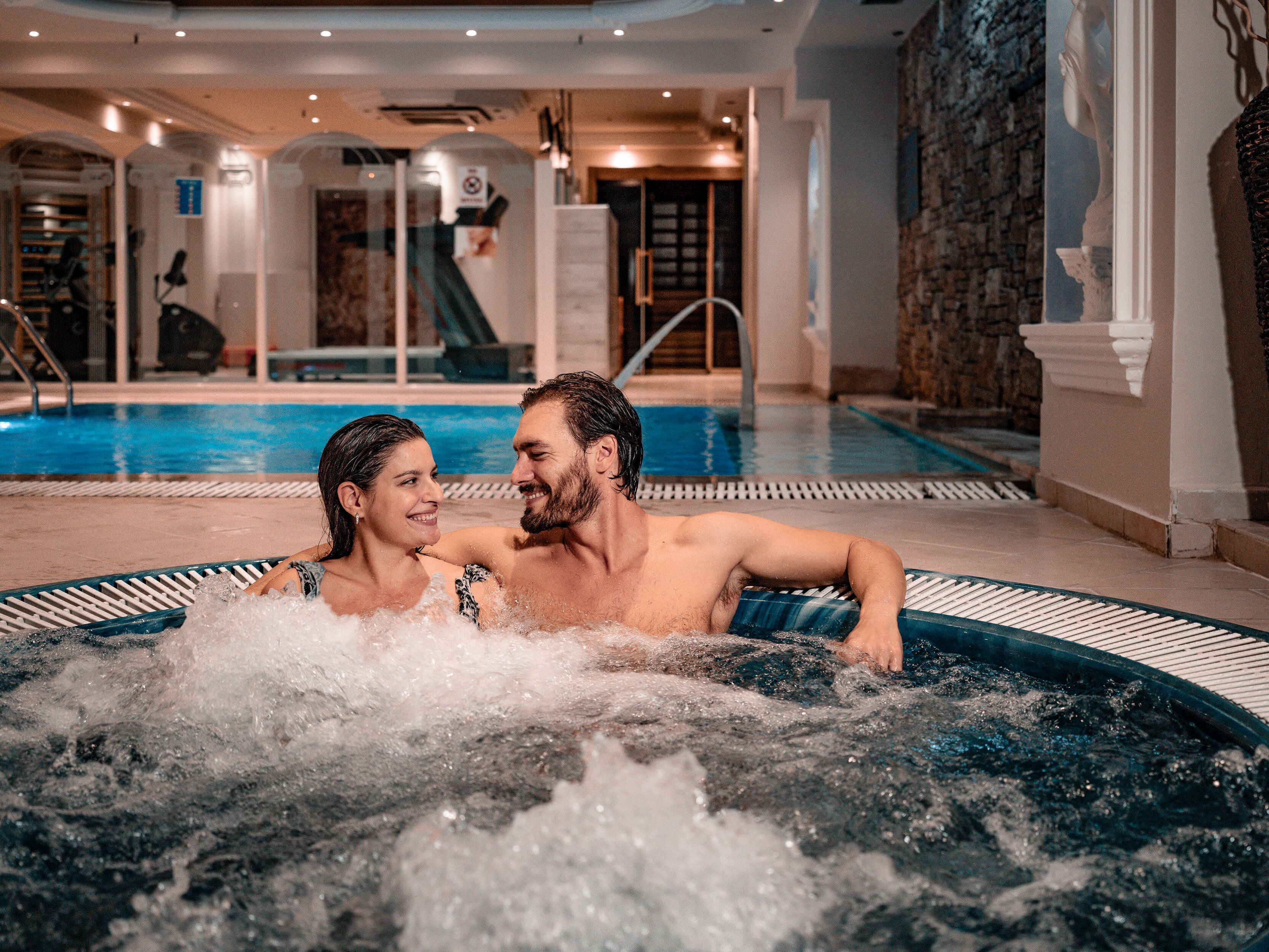Una pareja en un jacuzzi con piscina y tobogán al fondo.