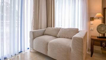 Una sala de estar moderna con un sofá color beige, cortinas traslúcidas, una mesita de madera con lámpara y una pared con textura.