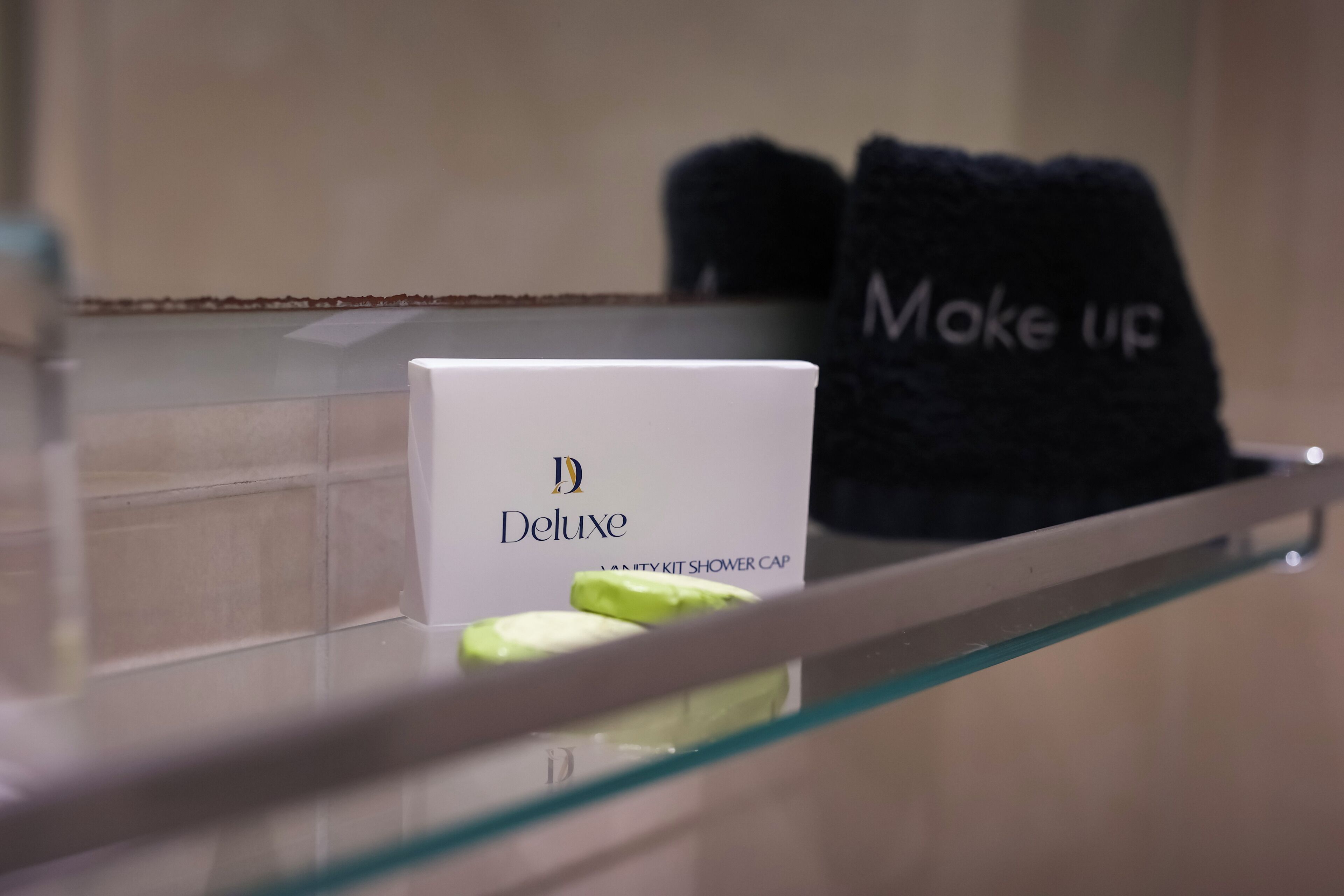 A bathroom with a glass shower enclosure, a white box labeled "Deluxe" and a black towel with "Moke Up" text.