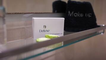 A bathroom with a glass shower enclosure, a white box labeled "Deluxe" and a black towel with "Moke Up" text.