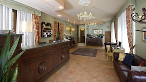 A spacious living area with a wooden reception desk, a leather sofa, a dining table with chairs, and a chandelier. - Hotel Villa Edera (Venice)