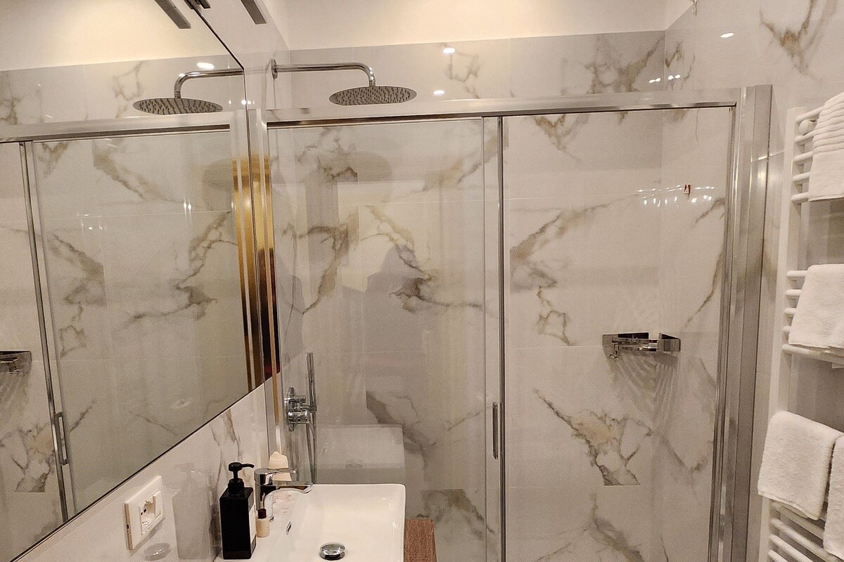 A modern bathroom with a glass-enclosed shower, a marble-tiled wall, and a wooden vanity with a sink.