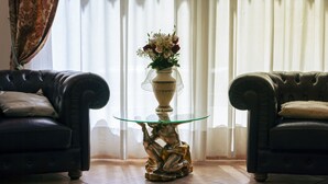A living room with two leather sofas, a glass-top coffee table with a decorative base, and a vase with flowers. - Hotel Villa Edera (Venice)