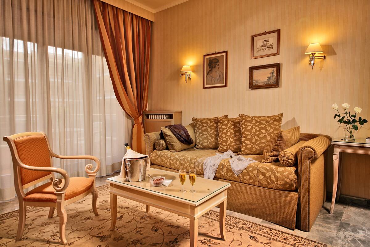 Ein Hotelzimmer mit einer Couch, einem Sessel und einem kleinen Tisch mit zwei Sektgläsern.