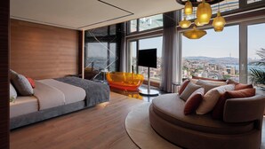 Een moderne woonkamer met een bank, een rond voetenbankje en een groot raam met uitzicht over de stad.