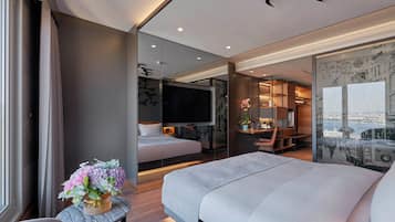 Habitación de hotel moderna con una cama grande, un escritorio, un televisor y vistas a la ciudad a través del muro de vidrio.