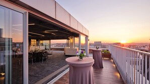Een terras op het dak met een eethoek, een bar en uitzicht op de ondergaande zon.