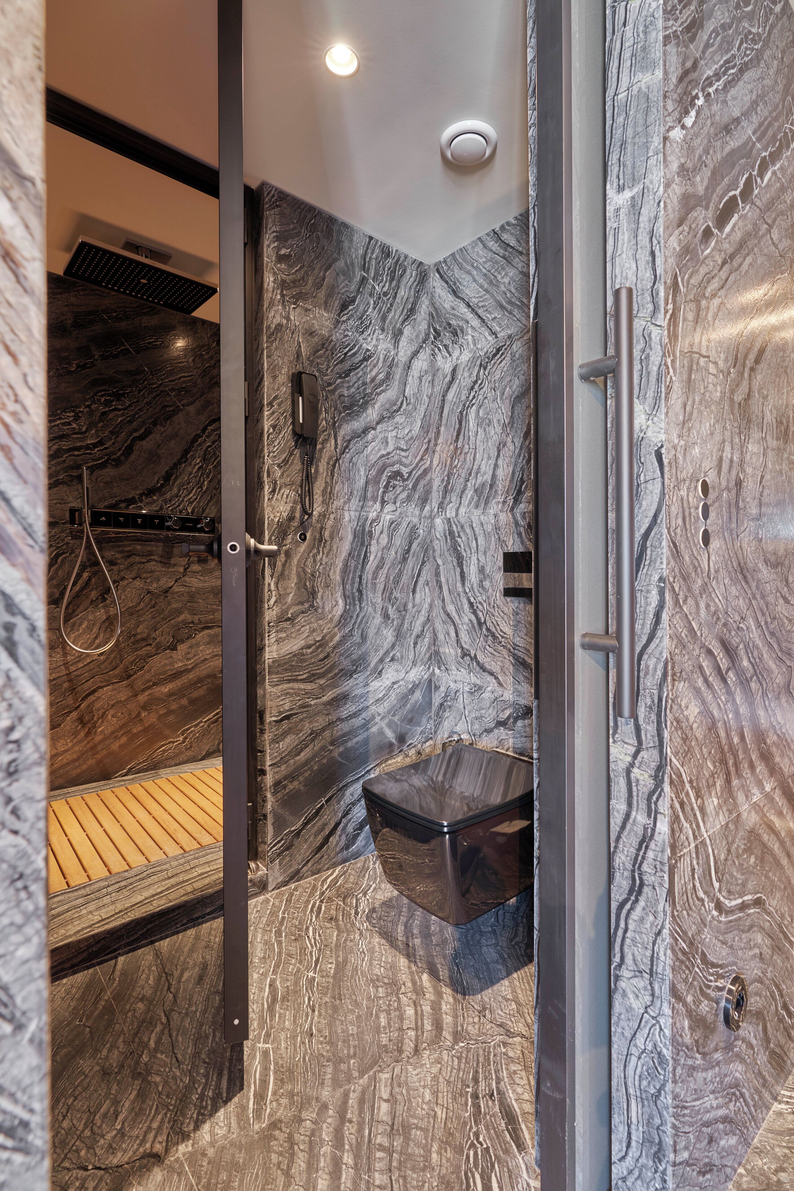A modern bathroom with a marble wall, a shower, and a glass-enclosed toilet.