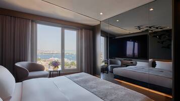 A modern hotel room with a large bed, a seating area with a small table, and a large window offering a city view.