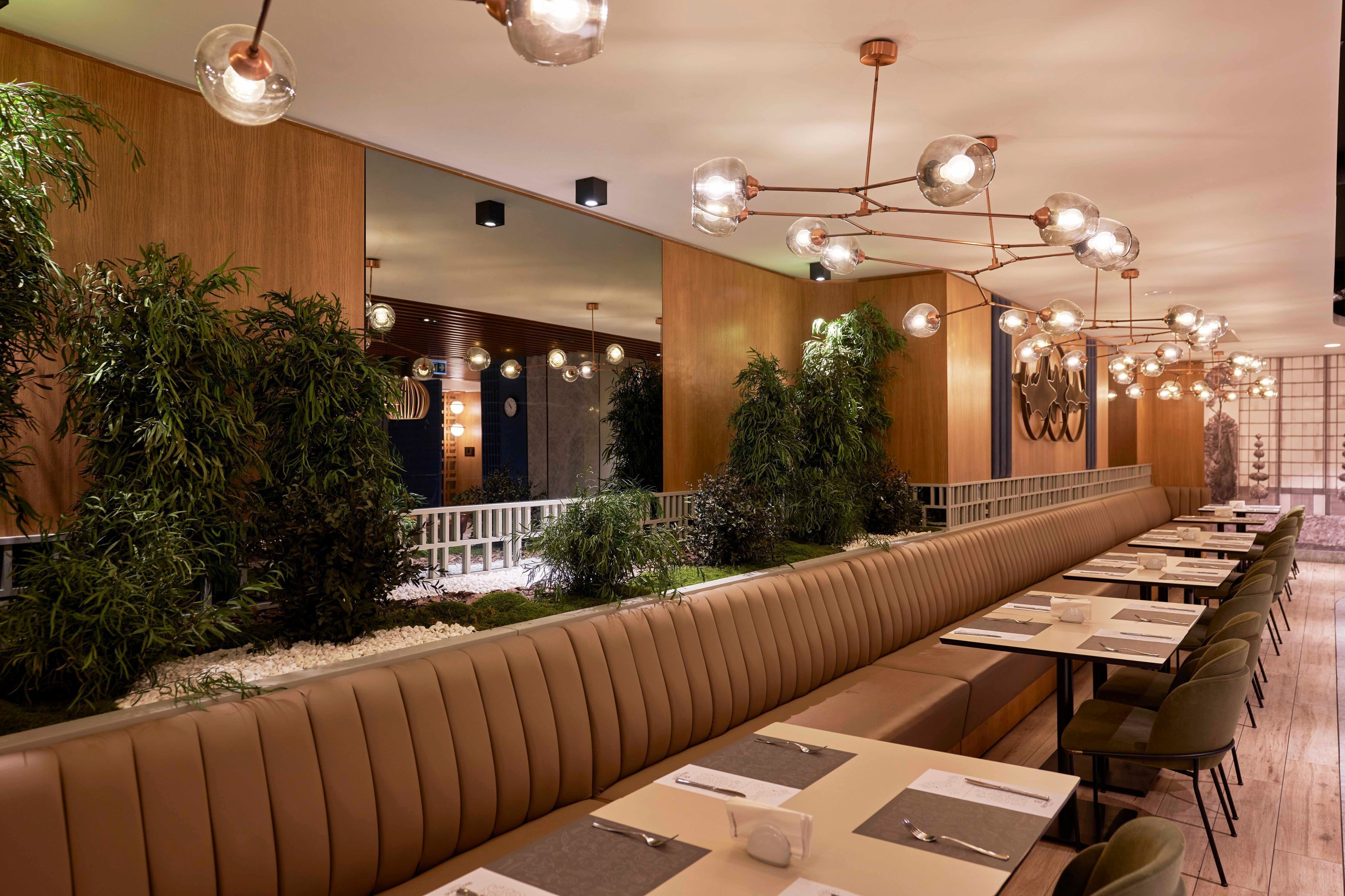 A long, modern dining area with a central bench, multiple tables, and ambient lighting.