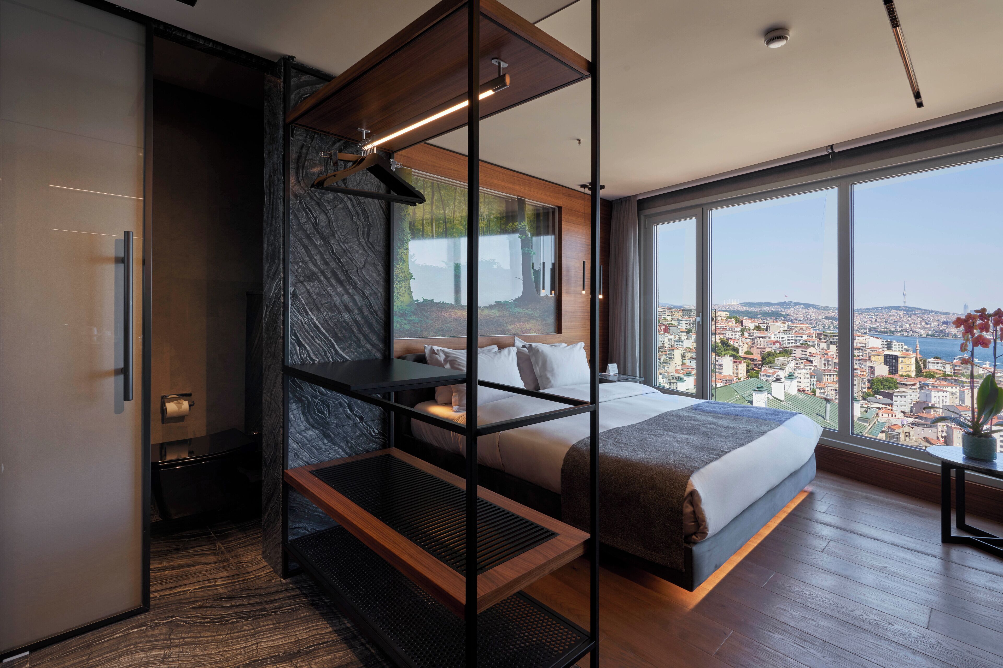 A modern hotel room with a large bed, a view of the city, and a unique shelving unit.