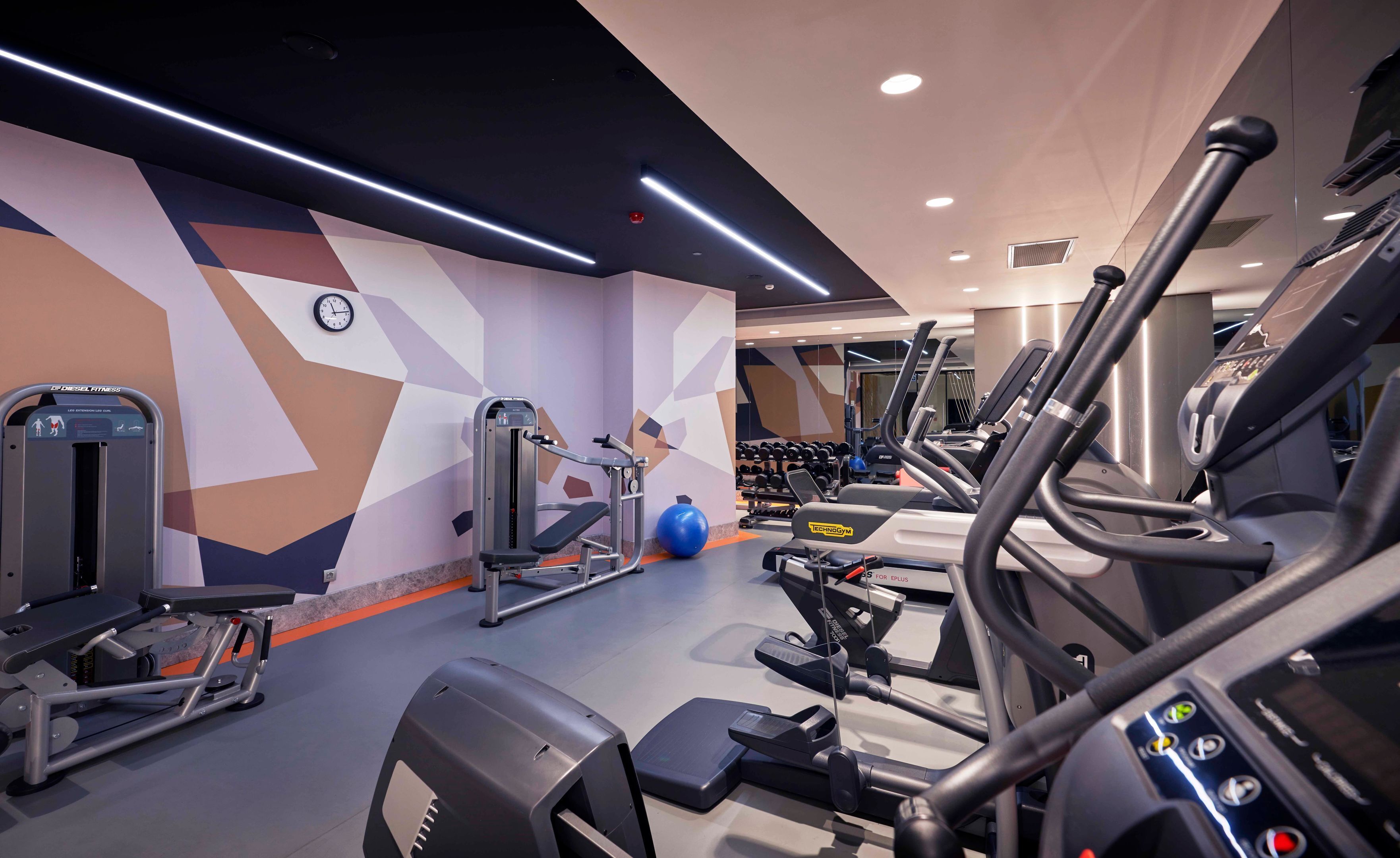 A modern gym with various exercise equipment, including treadmills, a weight machine, and free weights.
