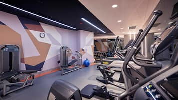 Een moderne sportschool met diverse fitnessapparaten, waaronder loopbanden, een gewichtstoestel en losse gewichten.