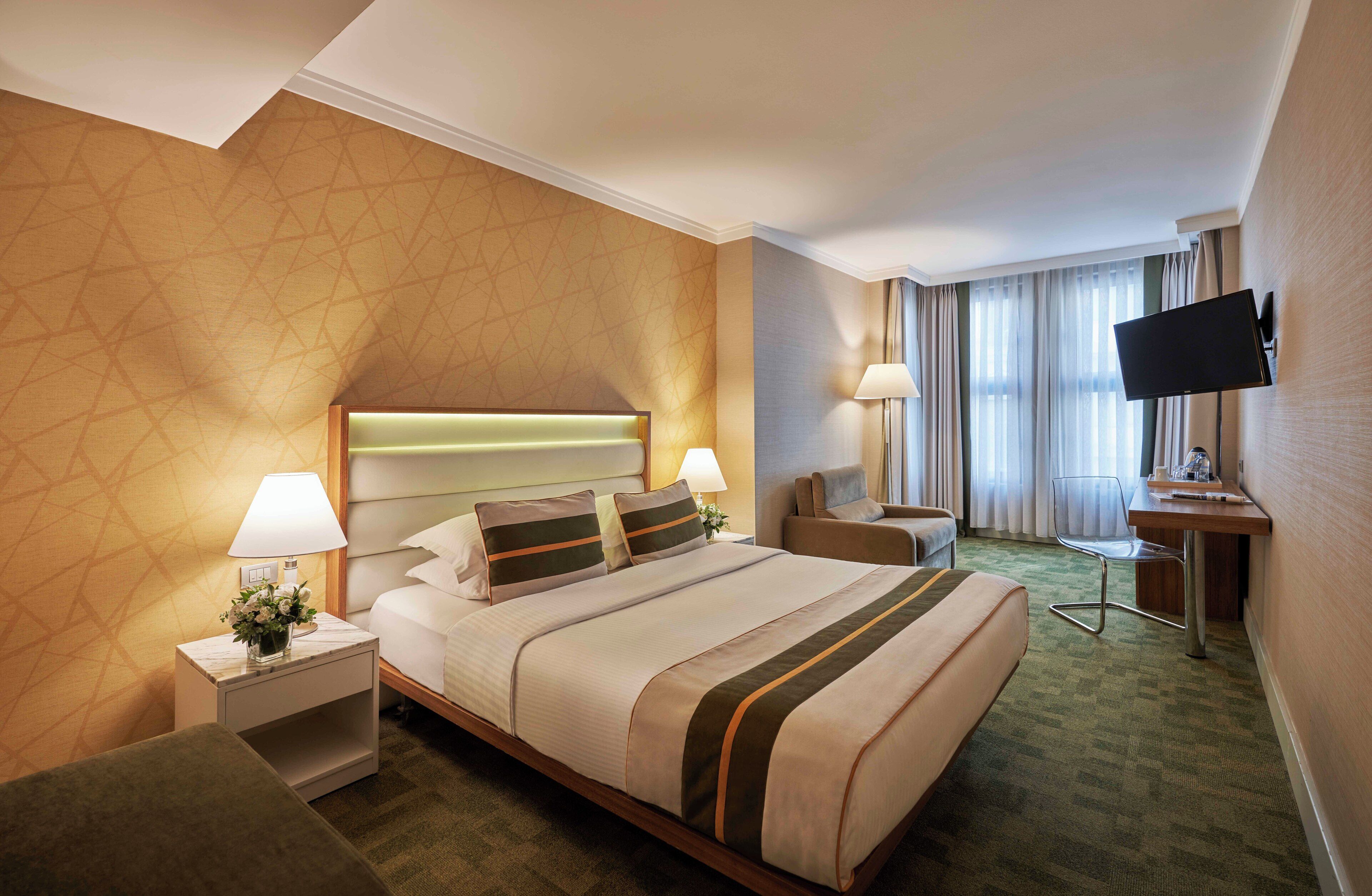 Een hotelkamer met een groot bed, twee nachtkastjes, een bureau, een stoel, een televisie en een raam met gordijnen.