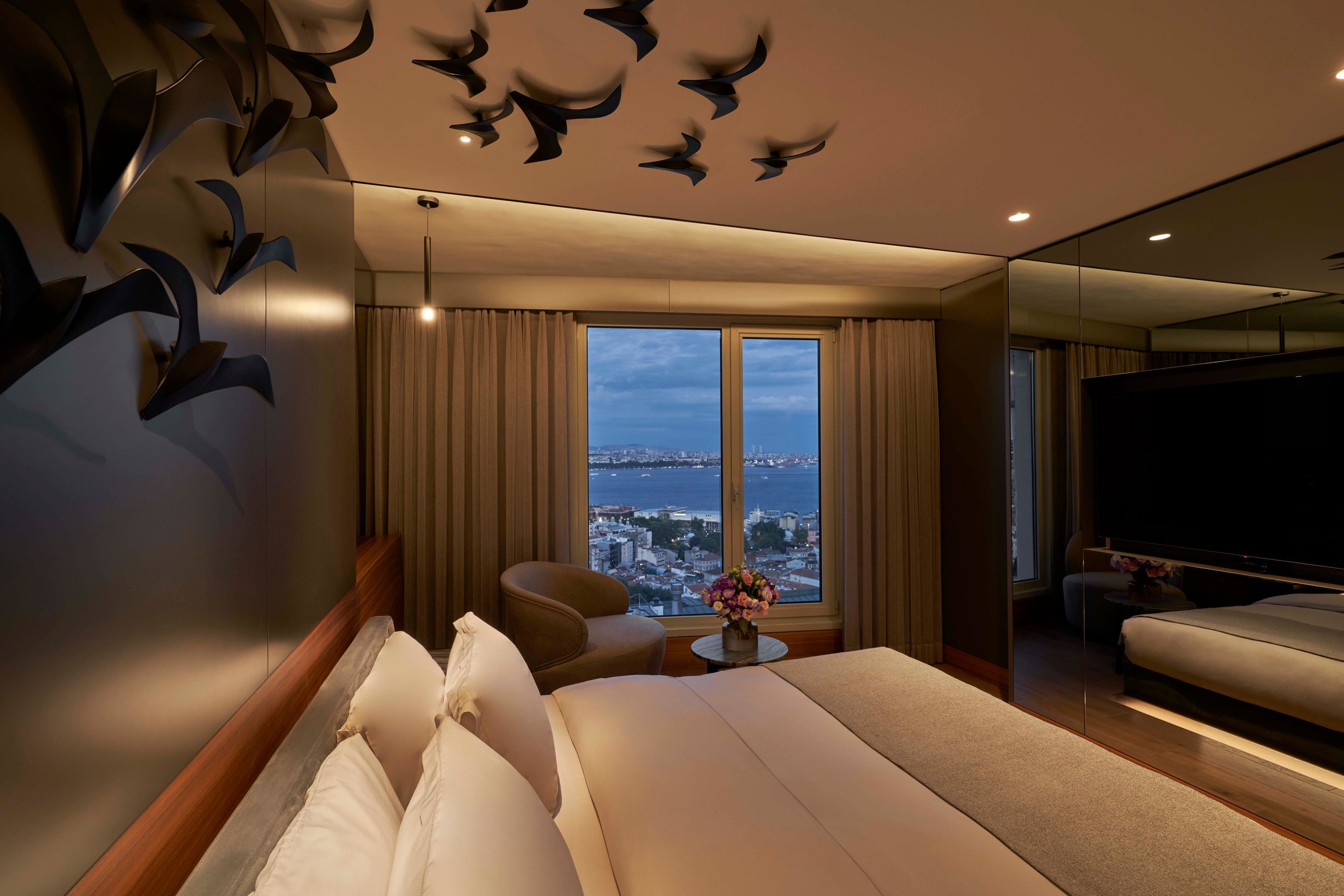 Une chambre d’hôtel moderne dotée d’un grand lit, d’un coin salon, d’une télévision et offrant une vue sur la ville par la fenêtre.