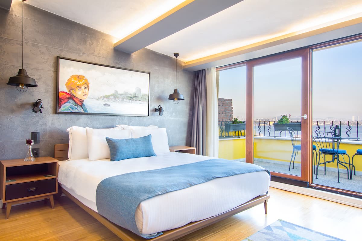 A modern hotel room with a large bed, a city view balcony, and a painting on the wall.