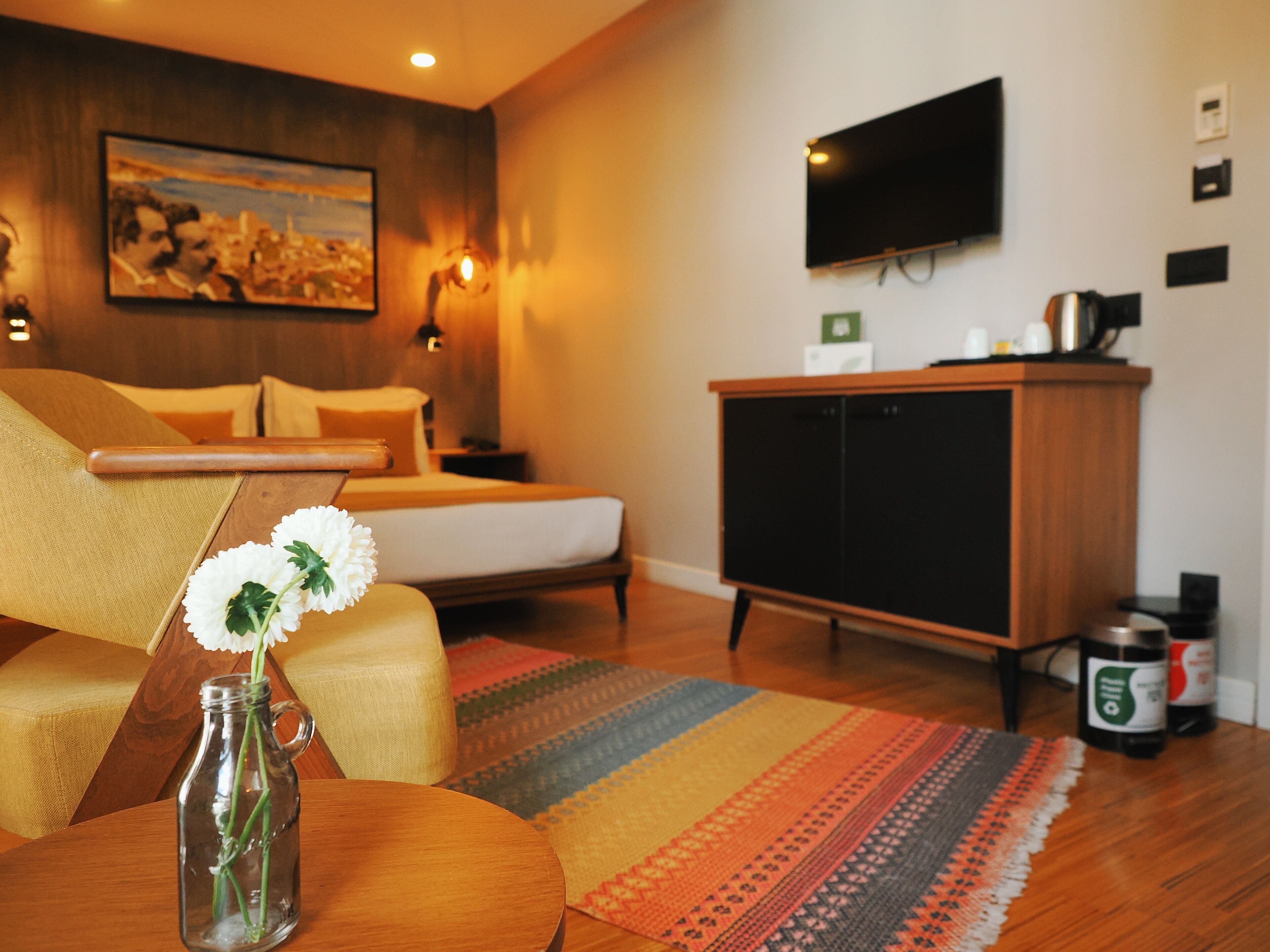 Una habitación de hotel moderna con una cama, un sofá, un televisor montado en la pared, un armario de madera y una alfombra decorativa.