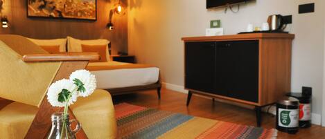 Una habitación de hotel moderna con una cama, un sofá, un televisor montado en la pared, un armario de madera y una alfombra decorativa.